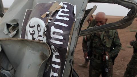 Peshmerga fighters inspect the remains of a car bearing an image of the trademark jihadist flag, north of Mosul, August 18, 2014. (AHMAD AL-RUBAYE/AFP/Getty Images)