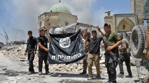 A member of the Iraqi Counter-Terrorism Service raises the victory gesture as others hold upside-down the black flag of the Islamic State in Mosul, Iraq, on June 30, 2017. (Fadel Senna/AFP via Getty Images)