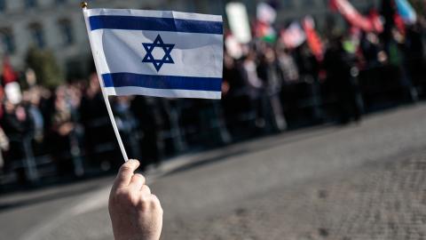 BERLIN, GERMANY - 2025/09/27: A protester holds an Israeli Flag during the counter demonstration. Tens of thousands of people marched in Berlin under the slogans "All Eyes on Gaza" and "Stop the Genocide," demanding a ceasefire, peace talks, and an end to German arms exports to Israel. Protesters carried Palestinian flags and banners, while police deployed 1,800 officers to maintain order. Organizers accused the German government of supporting Israel's actions in Gaza, which they descr