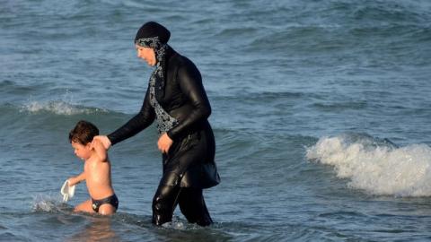 A Tunisian woman wearing a 'burkini' walks in the water with a child on August 16, 2016 at Ghar El Melh beach near Bizerte, north-east of the capital Tunis. (FETHI BELAID/AFP/Getty Images)